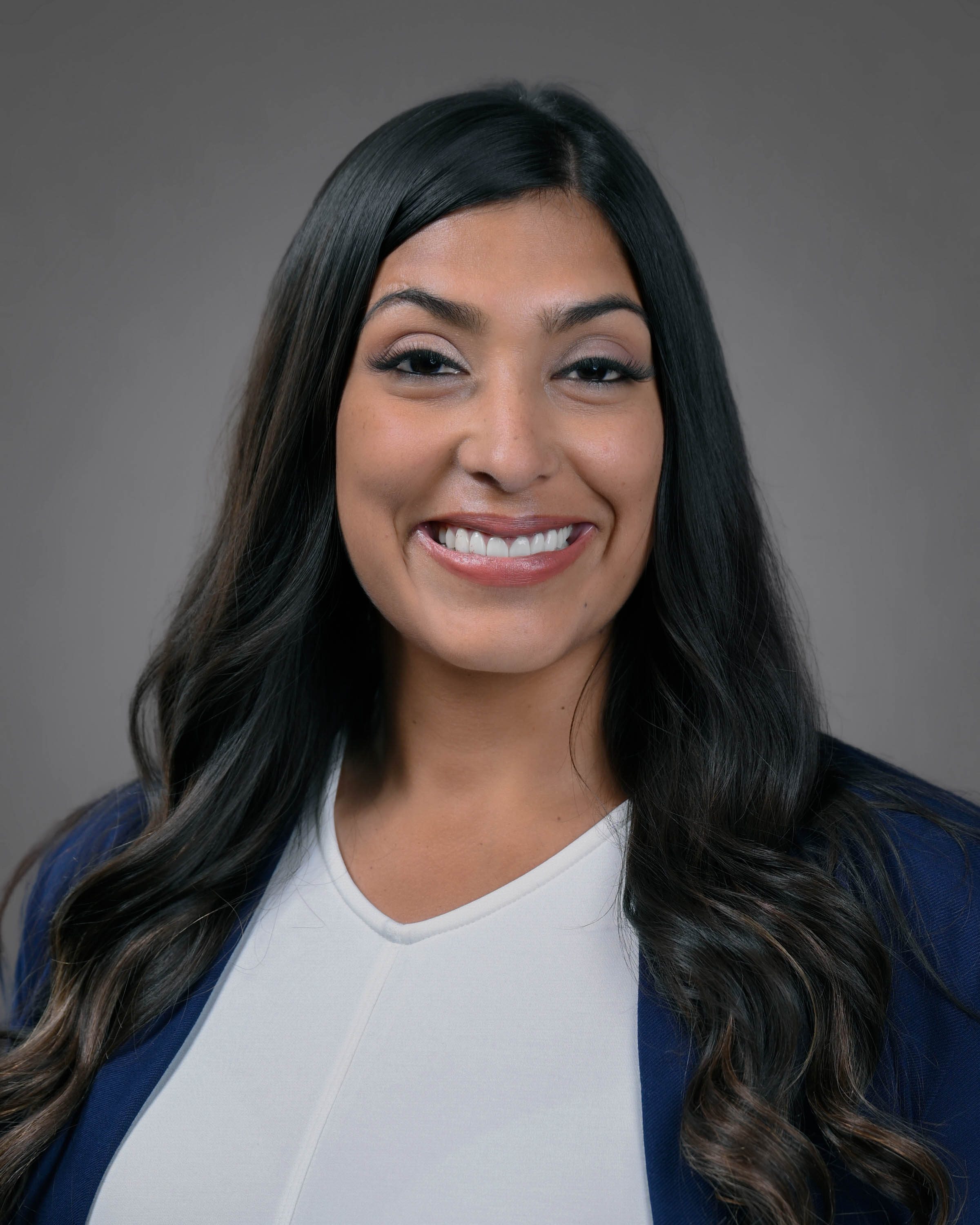 Smiling woman with long dark and slightly curly hair wearing a blue jacket and white shirt.